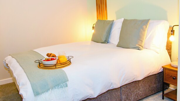 Una cama bien hecha con una bandeja de desayuno, almohadas y lámparas de noche.