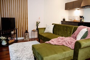A living room with a green sofa, a flat-screen TV, a patterned rug, and a kitchen in the background. - Stunning 1-bed Apartment in Sheffield City Centre (Sheffield)