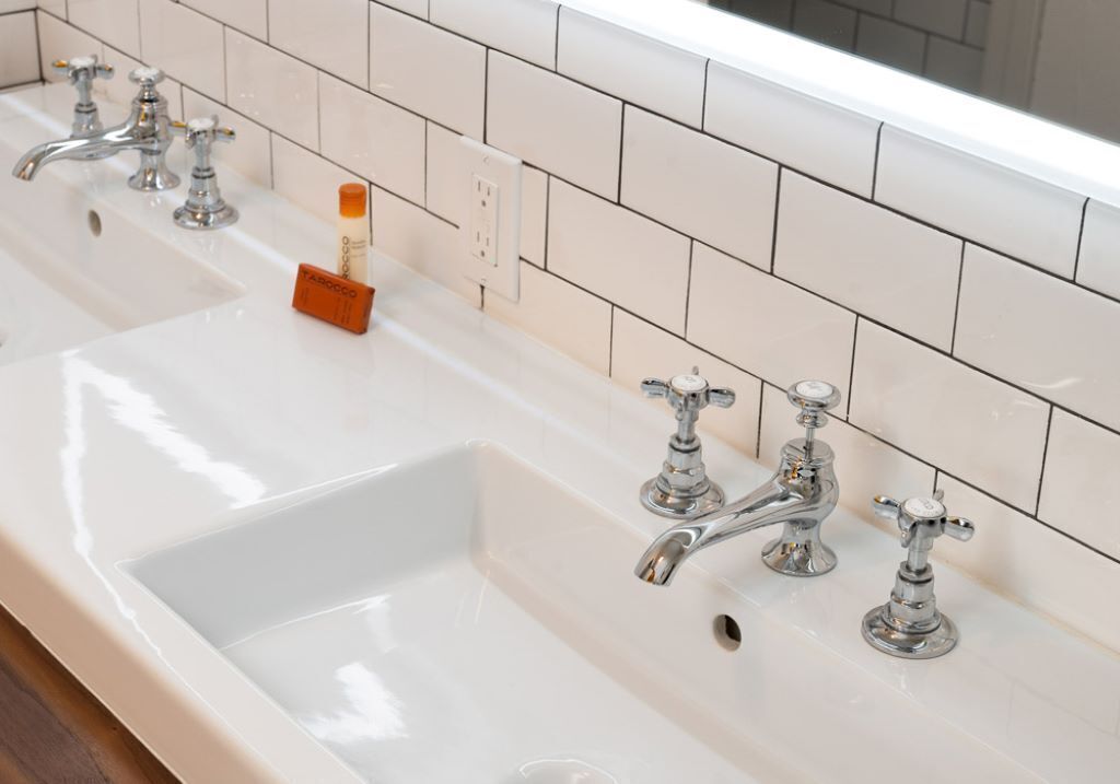 Baño con varios lavamanos y grifos, dispensador de jabón y perchero para toallas.