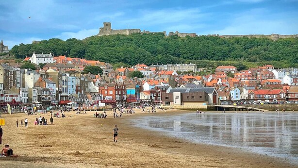 A beach with a historic castle in the background, a sandy shore, and a town with colorful buildings. - Stylish Apartment with views, lift and parking (Scarborough)