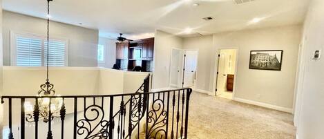 A spacious living area with a high ceiling, a staircase with ornate black railings, and a chandelier.