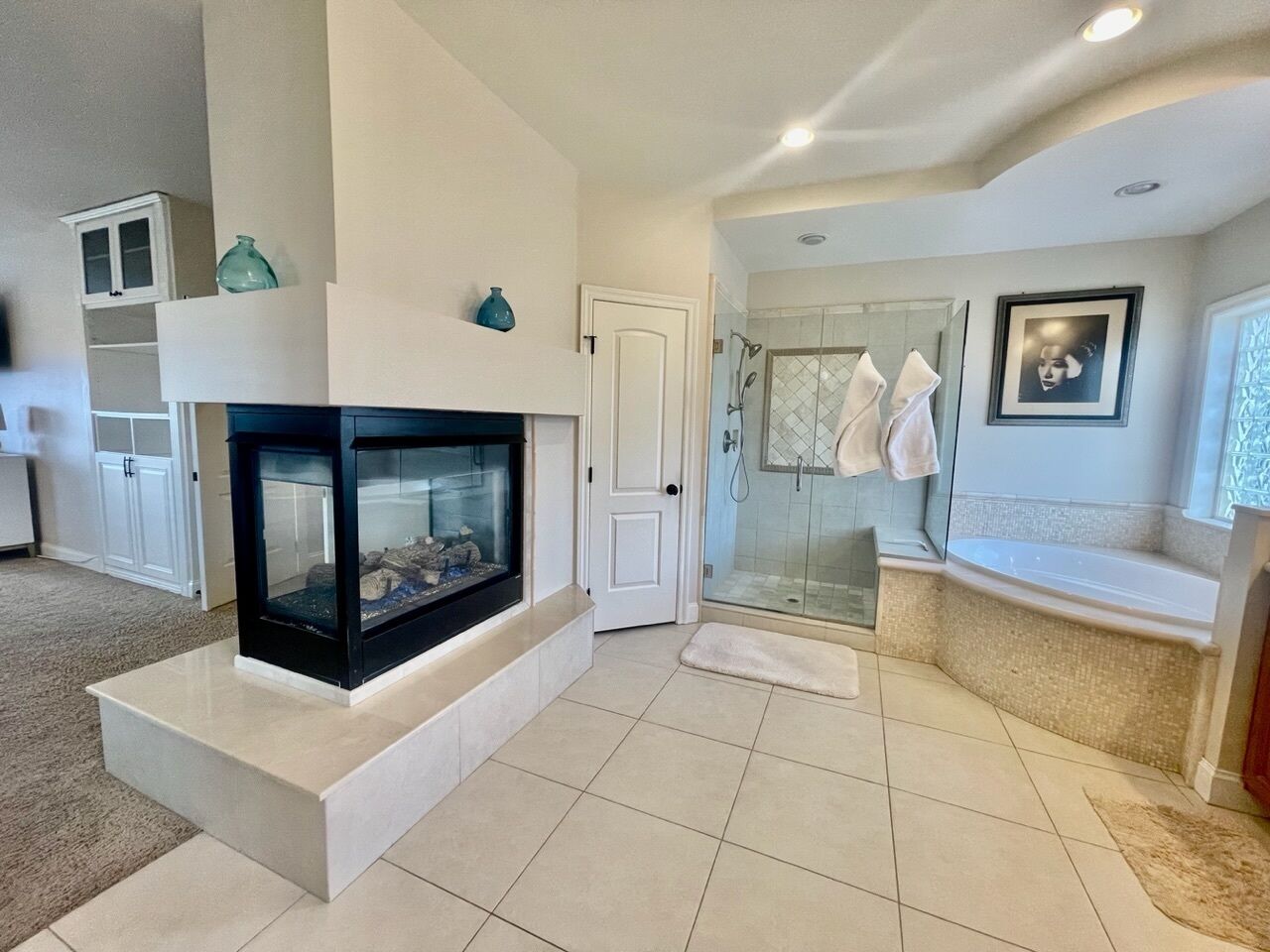 A modern bathroom with a glass shower, a bathtub, and a fireplace.