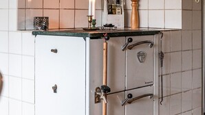 A kitchen with a white refrigerator, a wooden broom, and a shelf with jars.