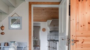 A hallway leading to a kitchen with a wooden door, a white cabinet with a vase, and a patterned rug.