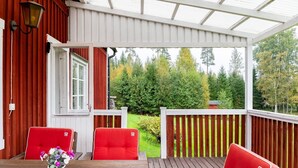 A covered outdoor seating area with two red cushioned chairs and a table with a vase of flowers.
