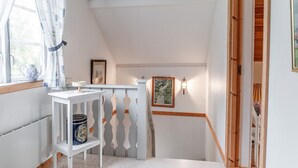 Un passadís estret i inclinat amb barana blanca, una taula petita amb un ram i un quadre penjat a la paret.