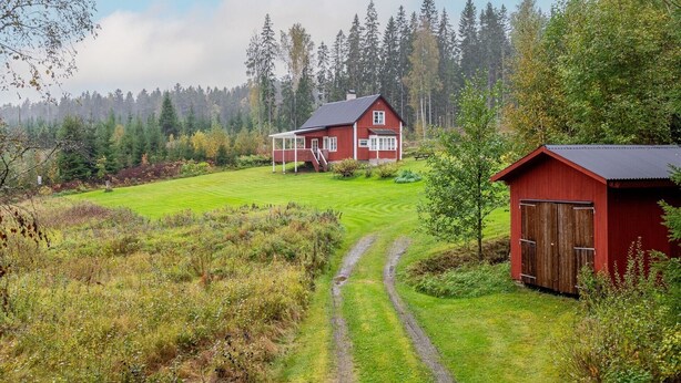 A red house with a porch, a barn, and a green field.