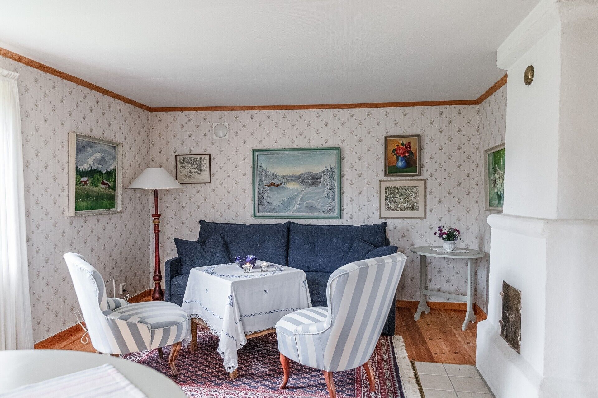A cozy room with a blue sofa, two striped chairs, a small round table, and a fireplace.