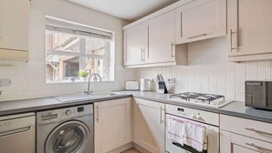 Una cucina compatta con mobili bianchi, una lavatrice integrata, un piano cottura a gas e una finestra che lascia entrare luce naturale.