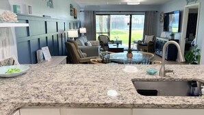 Una cocina moderna con encimeras de granito, un lavamanos integrado y un comedor con una mesa redonda de vidrio y sillas.