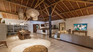 A spacious living area with a high ceiling, a dining table, and a television. - Villa Bahia Sol - Trancoso  (Porto Seguro)