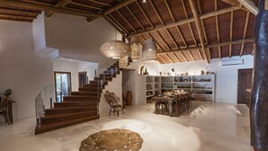 A spacious living area with a polished floor, a woven rug, a staircase, and a dining area with a wooden table and chairs. - Villa Bahia Sol - Trancoso  (Porto Seguro)
