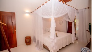 A bedroom with a canopy bed, wooden door, and a small drum. - Villa Bahia Sol - Trancoso  (Porto Seguro)