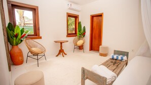 A room with a bed, two wicker chairs, a small round table, and a large potted plant. - Villa Bahia Sol - Trancoso  (Porto Seguro)