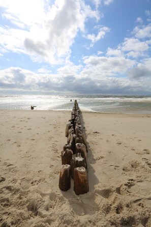 A beach with a wooden groyne extending into the sea, sandy beach, and a partly cloudy sky.
