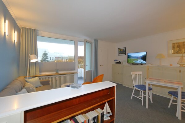 Une pièce confortable avec un canapé, une table à manger, un téléviseur et une bibliothèque.