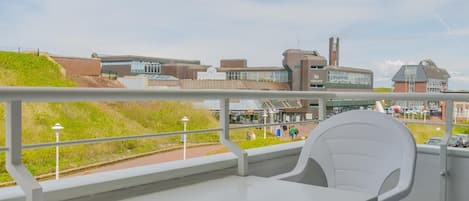 Ein Balkon mit weißem Tisch und Stühlen, der auf einen Campus mit Gebäuden und einer Grünfläche blickt.