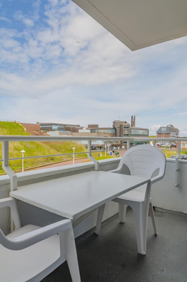 A balcony with a white table and chairs, overlooking a campus with buildings and a grassy area.