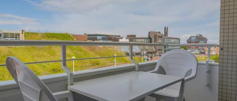 A balcony with a white table and chairs, offering a view of a grassy area and buildings in the background.
