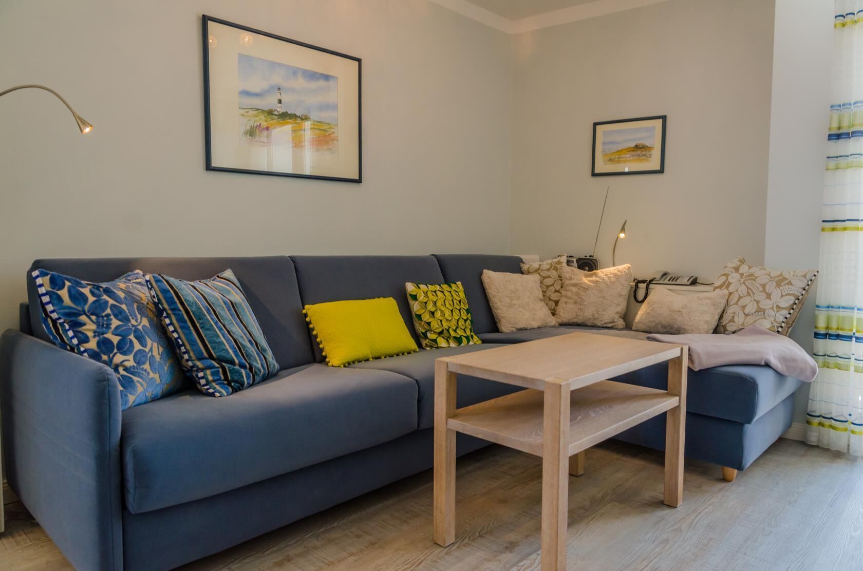 Una sala de estar con un sofá gris, una mesa de centro de madera y dos obras de arte enmarcadas en la pared.