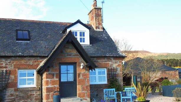A stone house with a black door, two windows, and a chimney.