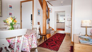 A dining area with a table set for two, a wooden staircase, and a kitchen visible through an open doorway.