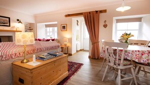A cozy living room with a sofa, a wooden chest of drawers, a dining table with chairs, and a kitchen area visible through an open door.