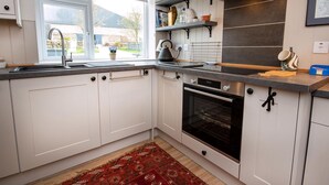 A modern kitchen with white cabinets, a built-in oven, a window with a view, and a red patterned rug.