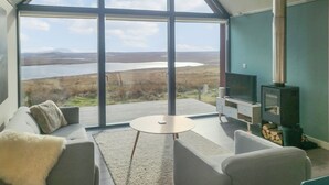 Ein modernes Wohnzimmer mit einem großen Fenster, das Blick auf einen See und Berge bietet.
