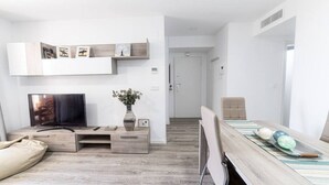 Un soggiorno moderno con una TV a schermo piatto, mobili in legno e una zona pranzo con tavolo e sedie.