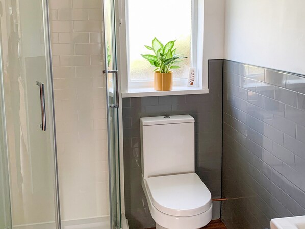 Un baño con inodoro, zona de ducha y una ventana con planta.