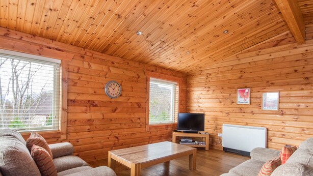 Ein rustikales Blockhaus-Interieur mit zwei Sofas, einem Holztisch, einem Fernseher und einer Whiteboard-Tafel.