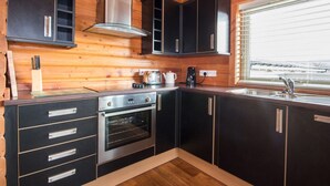 Eine moderne Küche mit Holzwänden, schwarzen Schränken, Edelstahlgeräten und einem Fenster mit Jalousien.