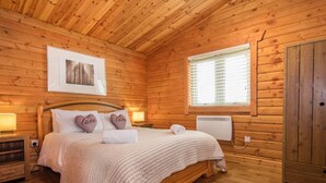 Ein gemütliches Schlafzimmer einer Holzhütte mit Bett, Nachttischlampen, Heizkörper und einem Fenster mit Jalousien.
