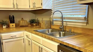 A kitchen with white cabinets, a stainless steel sink, wooden countertops, and a dishwasher.