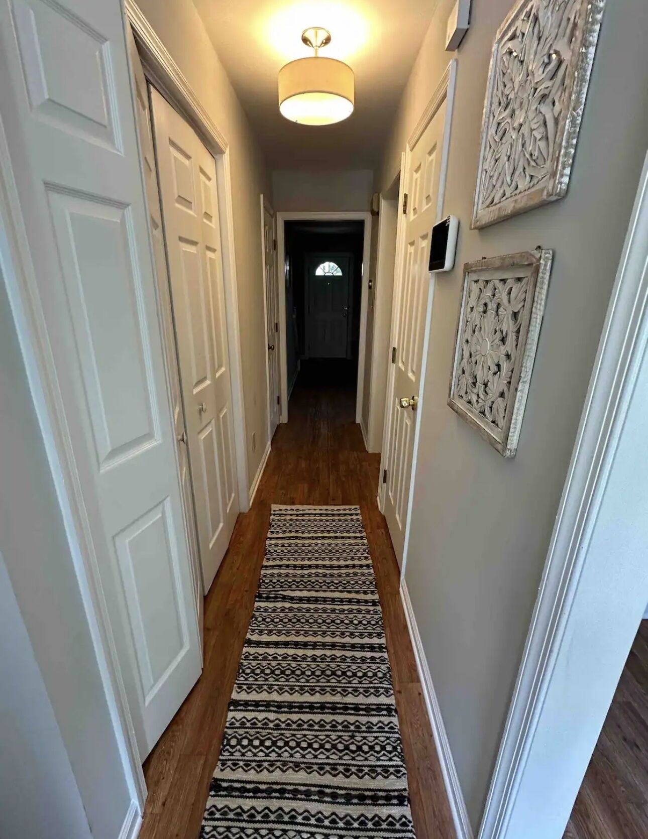 A hallway with white doors, a patterned rug, and decorative wall art.