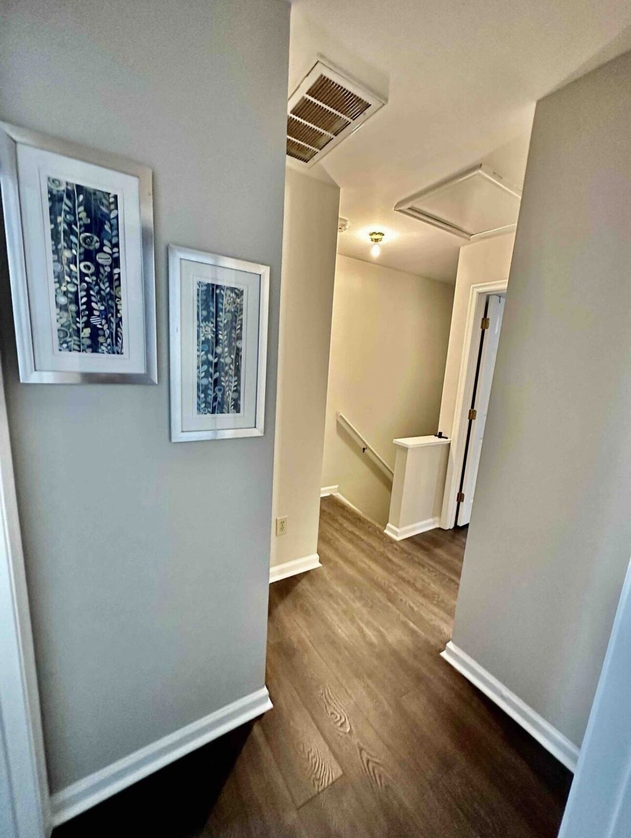 A hallway with wooden flooring, white walls, and two framed artworks.