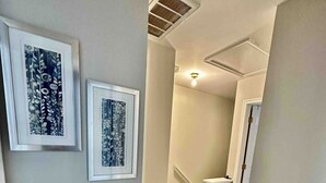 A hallway with wooden flooring, white walls, and two framed artworks.