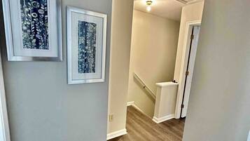 A hallway with wooden flooring, white walls, and two framed artworks.