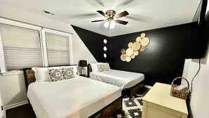 A bedroom with two beds, a ceiling fan, a wall-mounted light fixture, and a bedside table with a basket.
