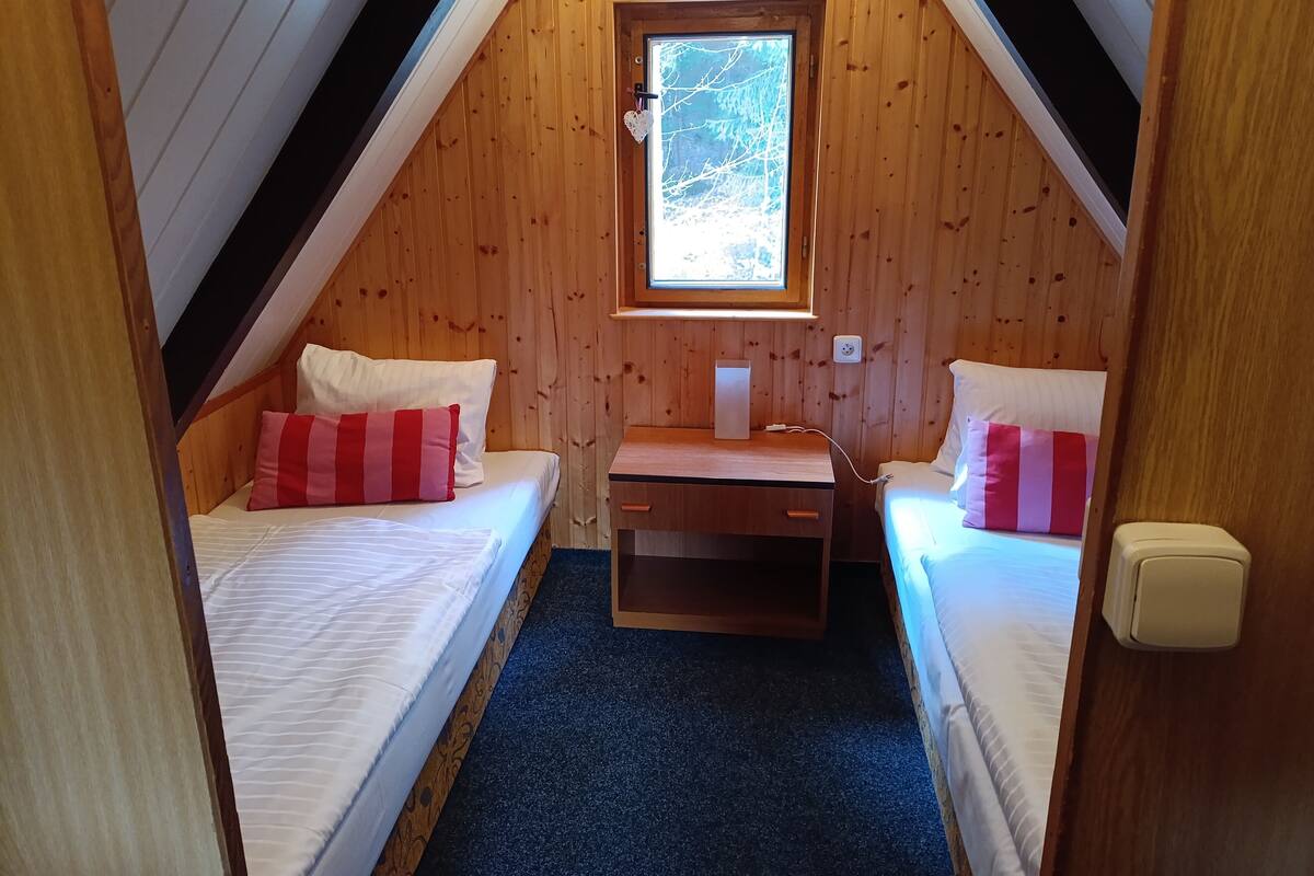 Un dormitorio acogedor en el ático con dos camas, un escritorio pequeño y una ventana.