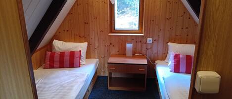 Un dormitorio acogedor en el ático con dos camas, un escritorio pequeño y una ventana.
