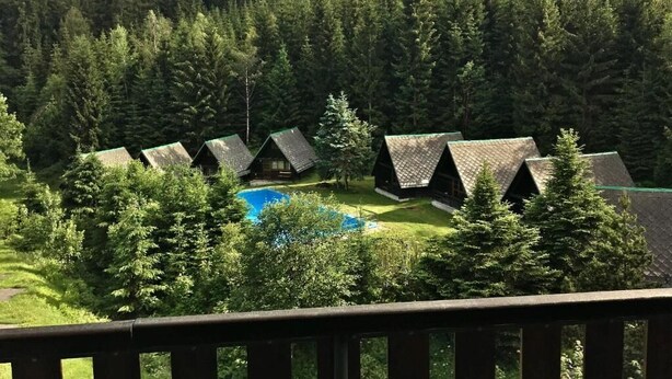 En række hytter med en swimmingpool i forgrunden, omgivet af tæt skov.
