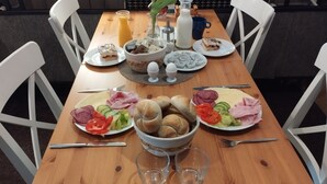 Et træbord med tallerkener med mad, herunder brød, grøntsager og kød. Der er også glas, et kande og en vase på bordet.