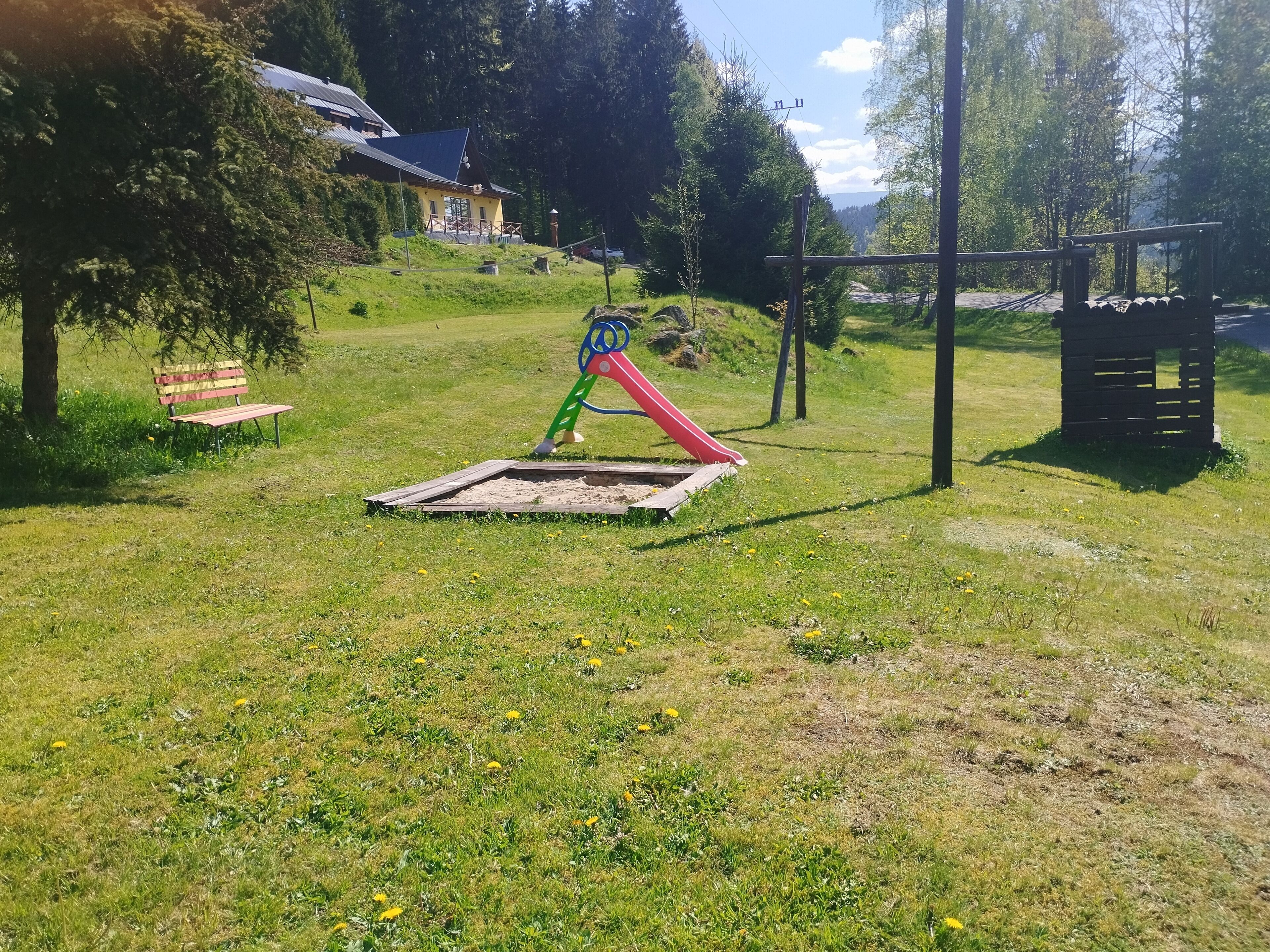 A playground with a slide and swings, surrounded by grass and trees.