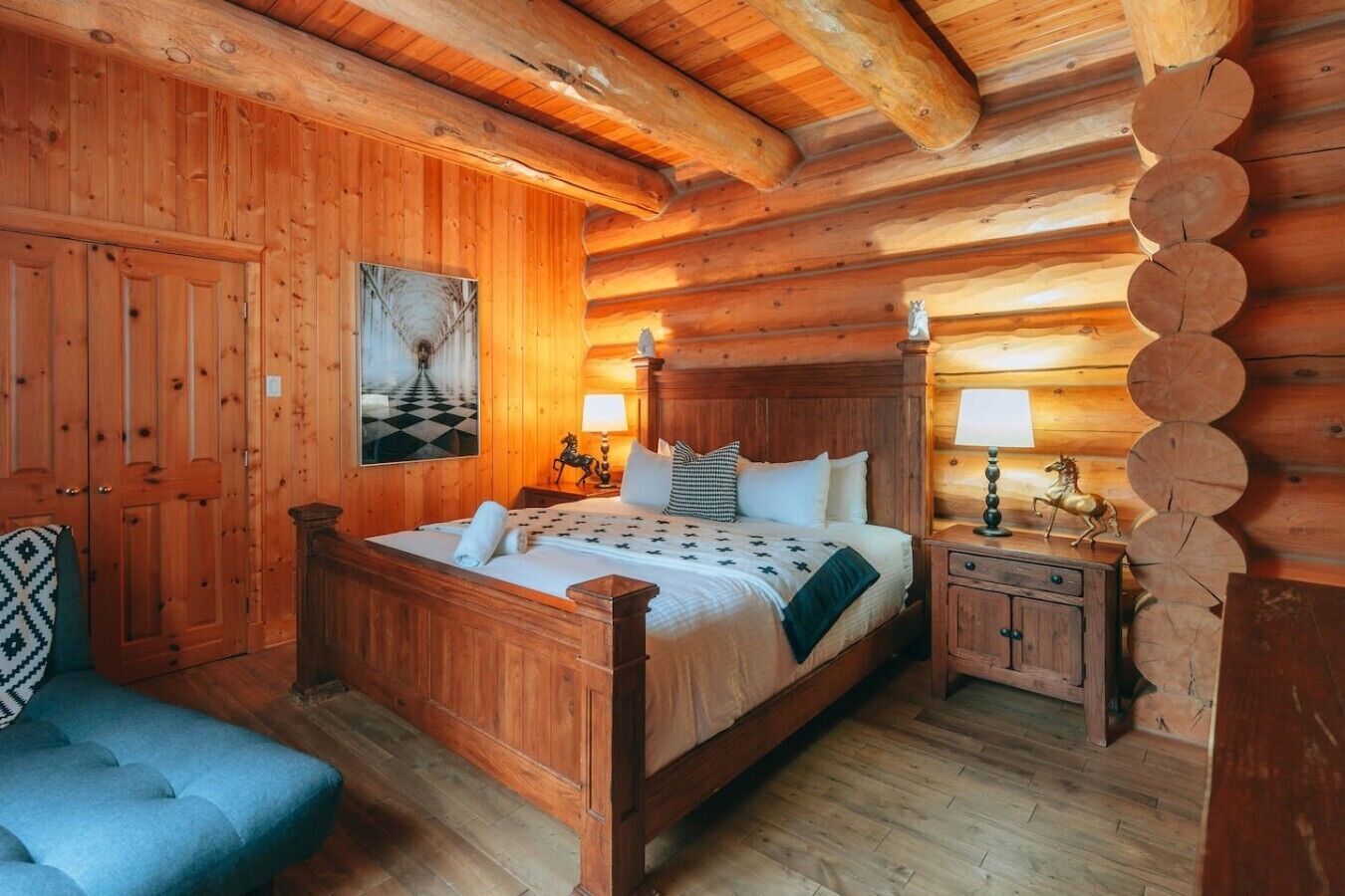 A wooden cabin room with a bed, a nightstand, a chair, and a wall-mounted lamp.
