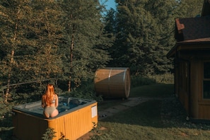 Een houten jacuzzi in een bebost gebied, met een vat en een klein houten gebouw.