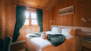 Un dormitorio de cabaña de madera con cama, cortinas, una lámpara de pared y una ventana.