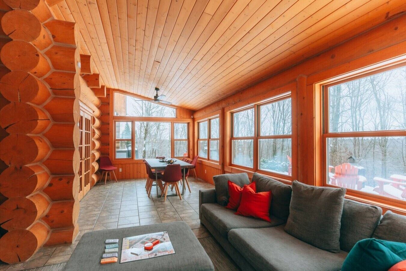 A log cabin interior with a dining area, a sofa, and large windows.