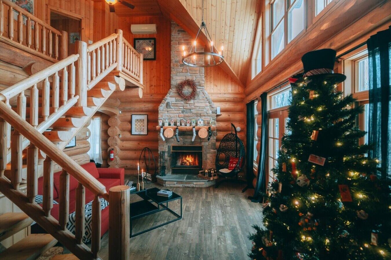 A log cabin interior with a fireplace, a Christmas tree, and a staircase.